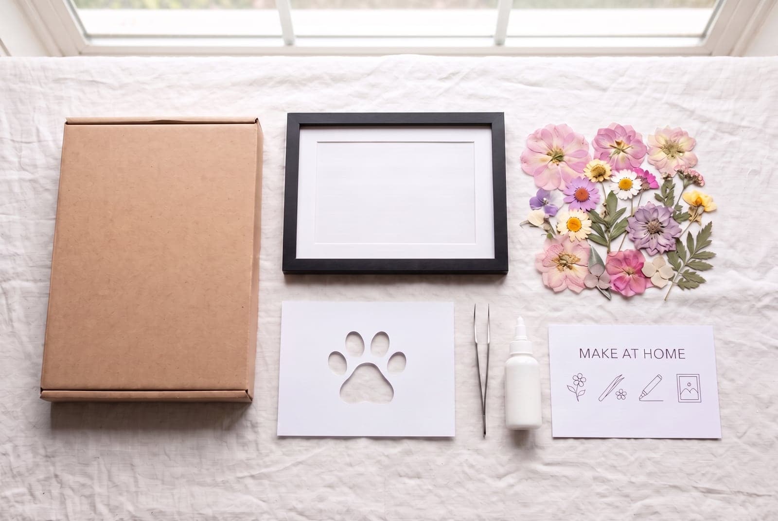Flat-lay of a complete pressed flower craft kit — frame, real pressed flowers, die-cut card stock, glue and tweezers